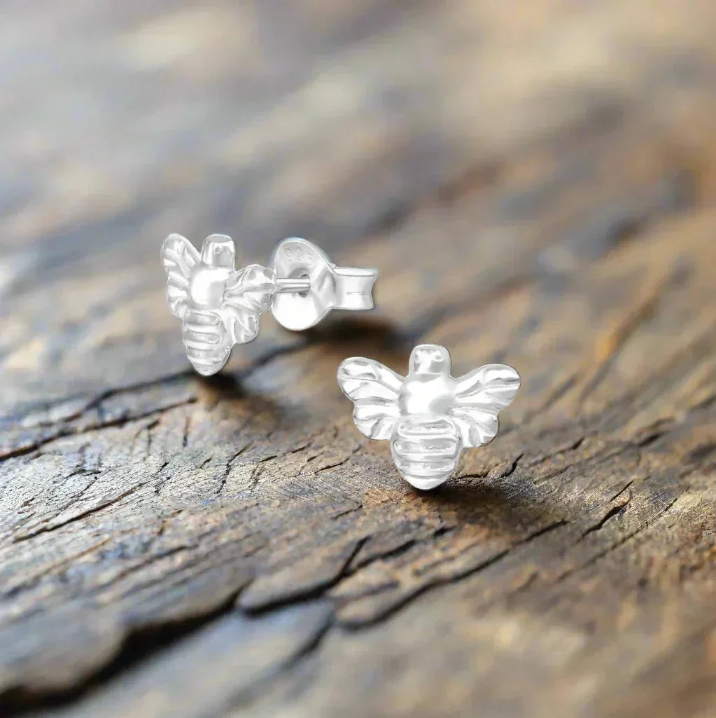 Sterling silver bee stud earrings on rustic wooden surface
