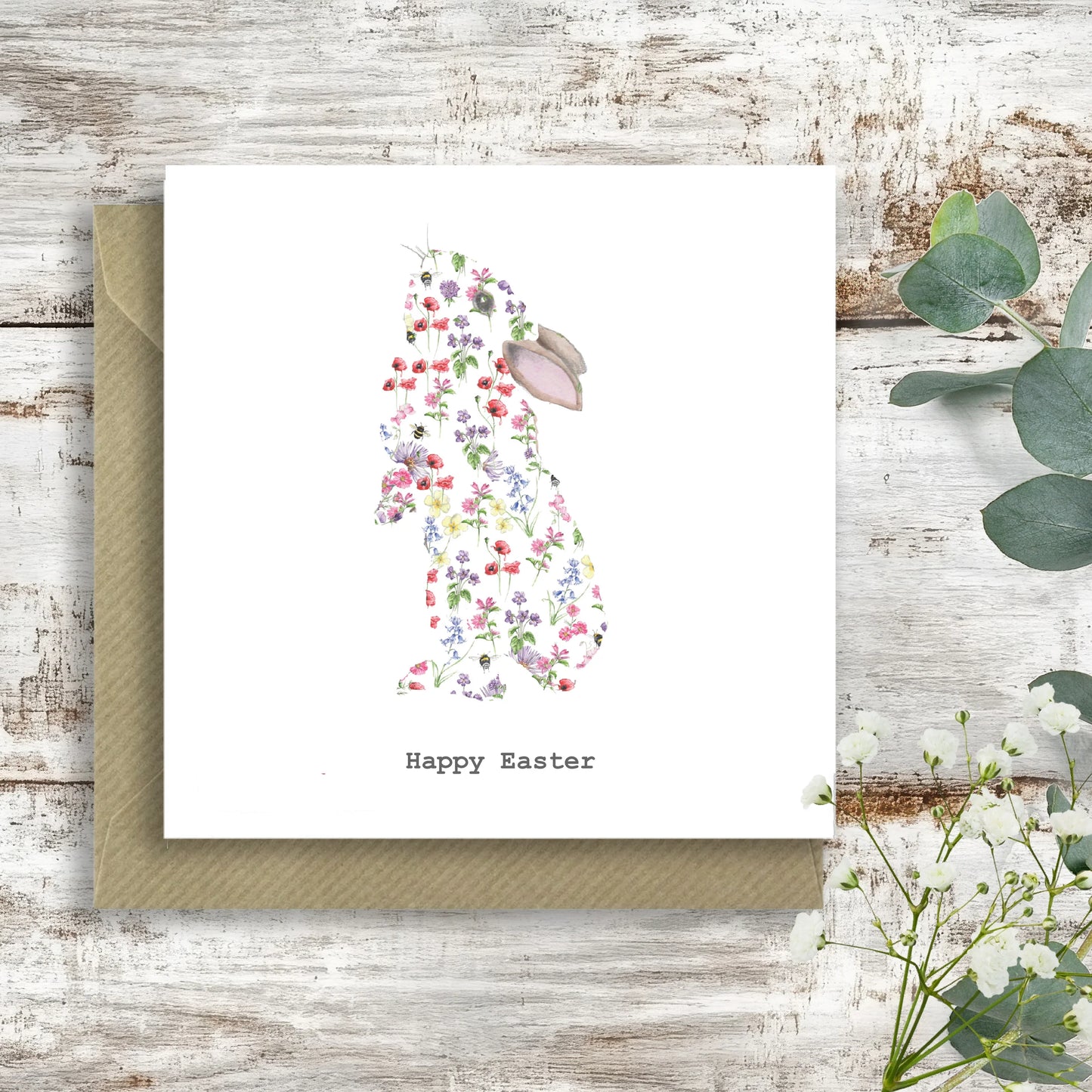 Floral bunny Easter card with 'Happy Easter' text, on rustic wooden background with foliage.
