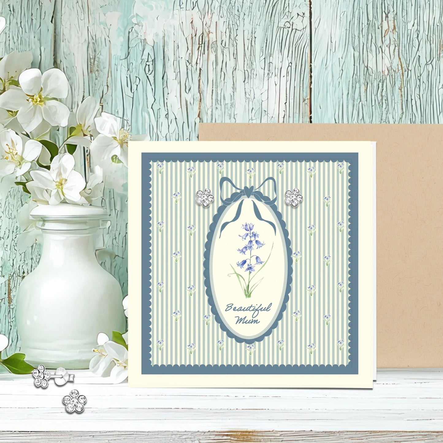 Floral greeting card for mum with delicate blue flowers, floral stud earrings, rustic background.
