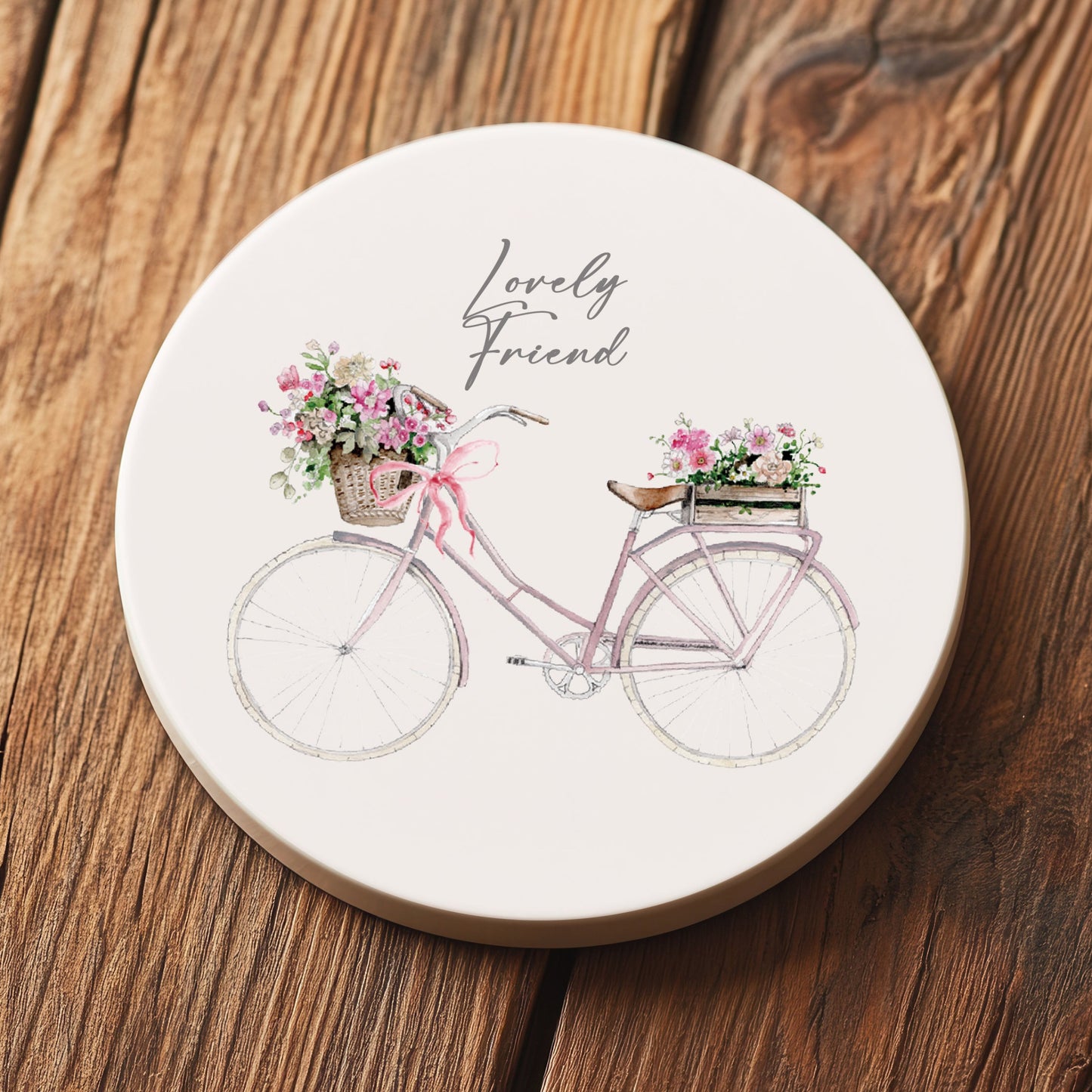 Ceramic coaster with pink bicycle, floral baskets, and 'Lovely Friend' text on wood surface