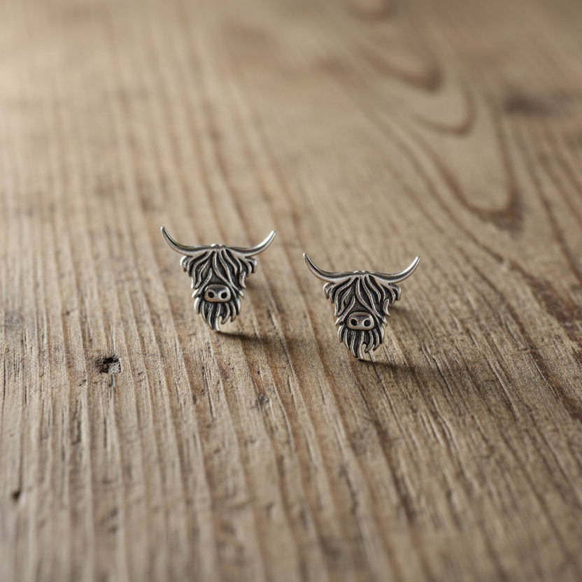 silver highland cow stud earrings on rustic wooden surface