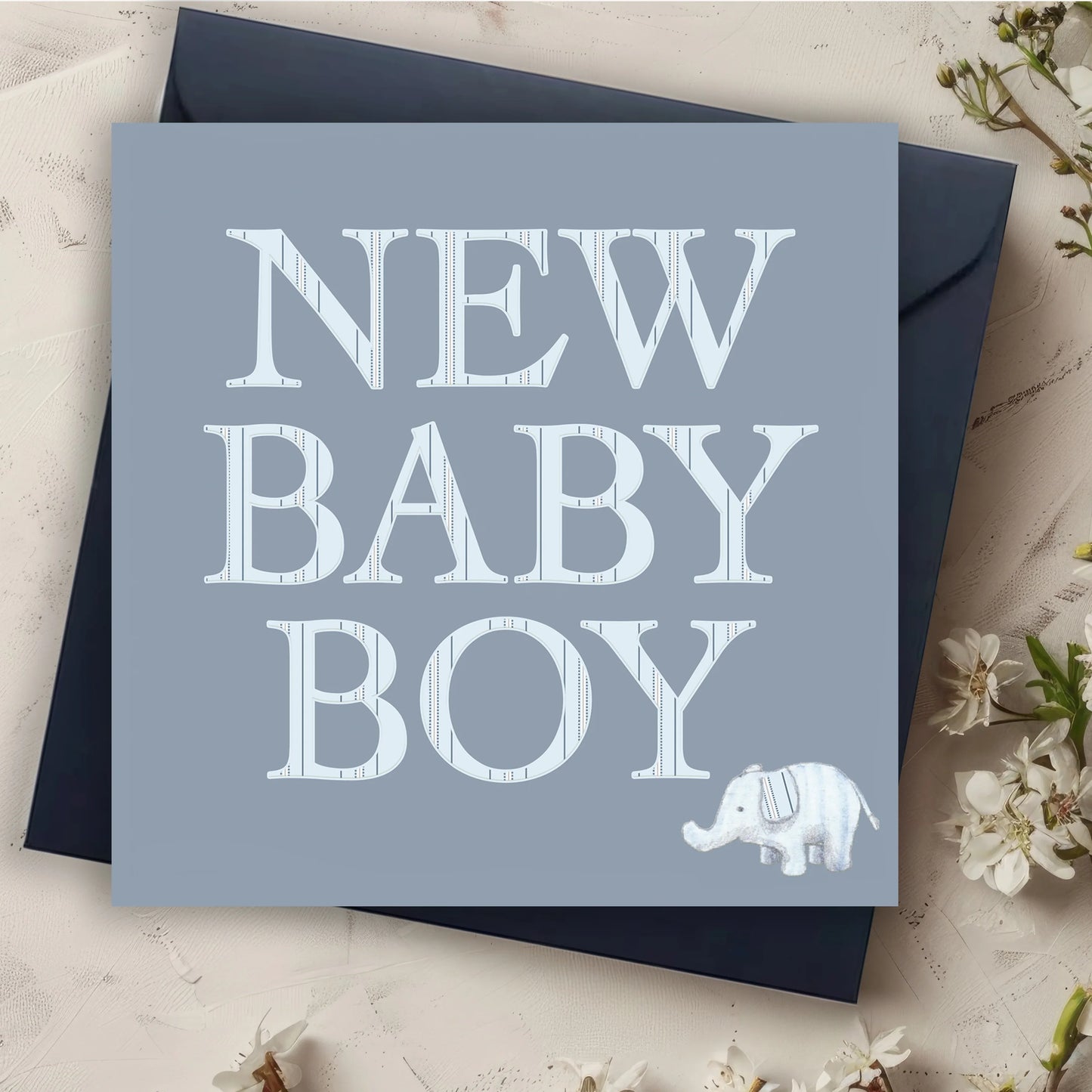 Blue new baby boy card with large white text and a small illustrated elephant, flowers nearby