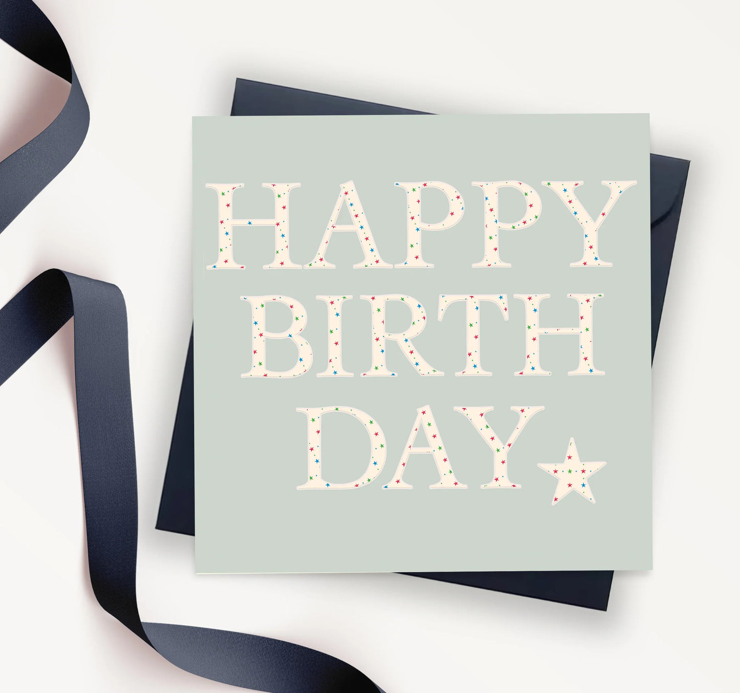 Happy Birthday card with pastel star confetti text, navy envelope and ribbon