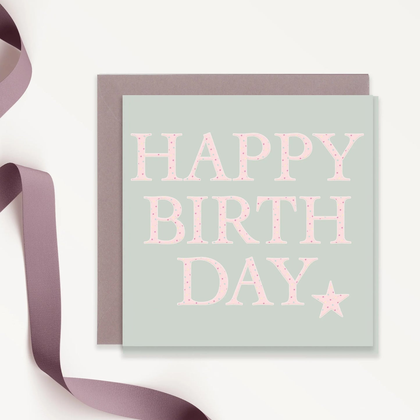 Pastel birthday card with pink polka dot lettering, grey envelope, and mauve ribbon