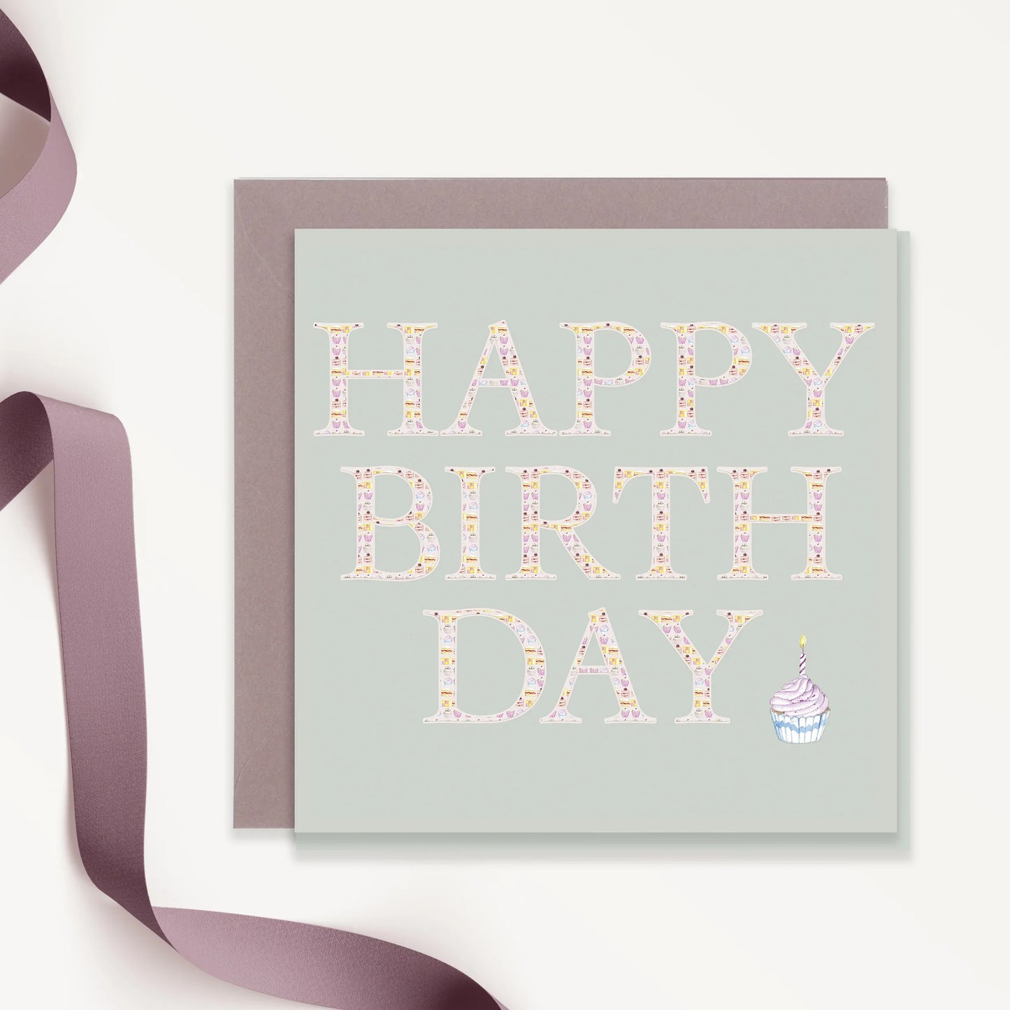 Happy Birthday card with pastel patterned letters and cupcake illustration, beside lavender ribbon