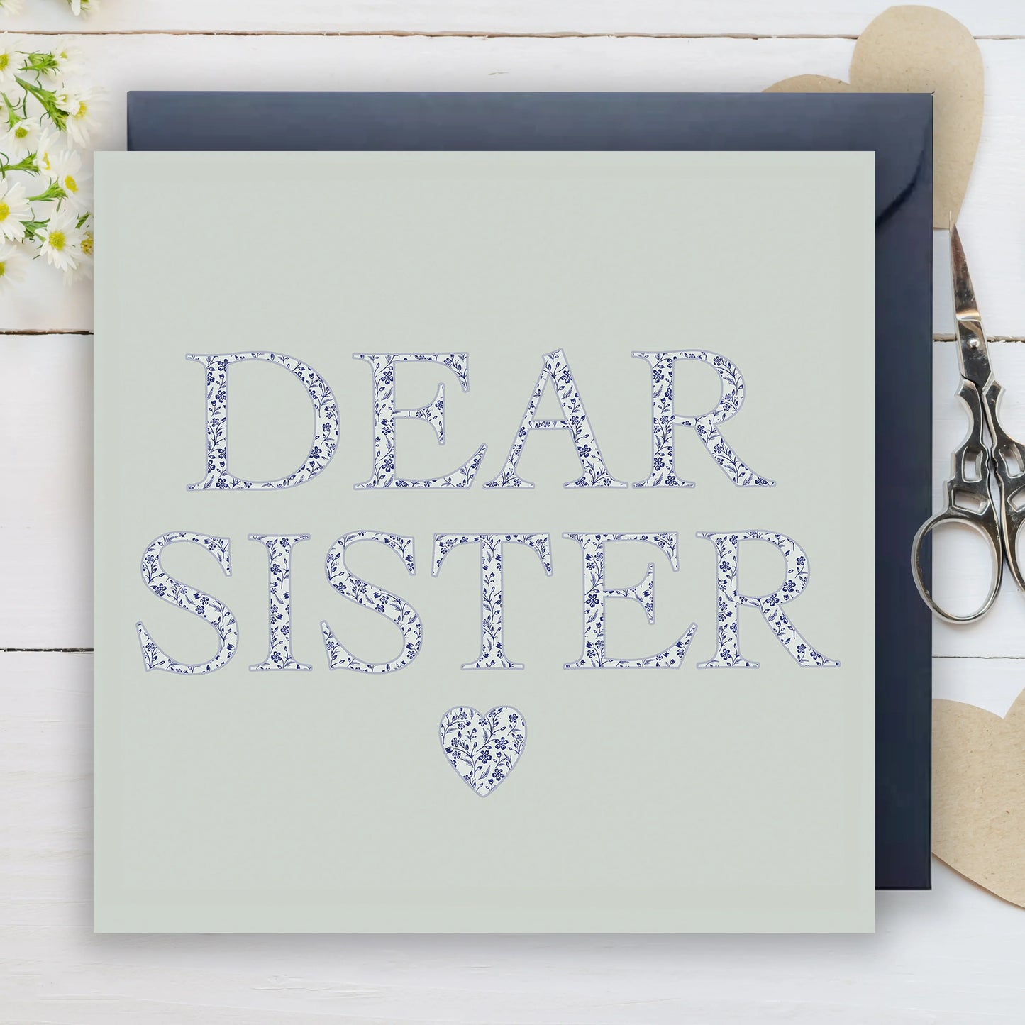 Floral Dear Sister greeting card with heart, navy envelope, and scissors on white wood