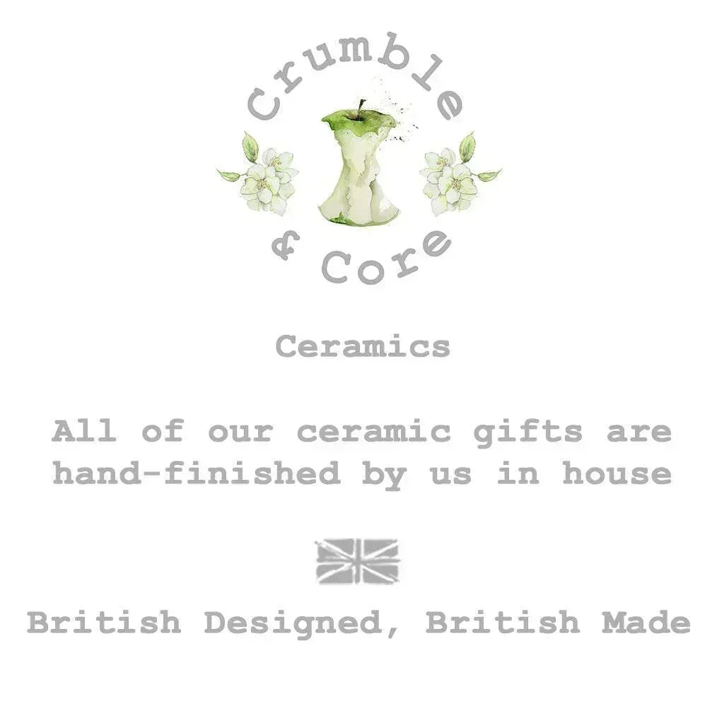 The image is a logo for a company called Crumble & Core, which specializes in ceramics. The logo features an apple with a green stem and leaves, surrounded by white flowers. The company's slogan, "All of our ceramic gifts are hand-finished by us in house", is displayed below the logo. The company's British-designed, British-made tagline is also included in the image.