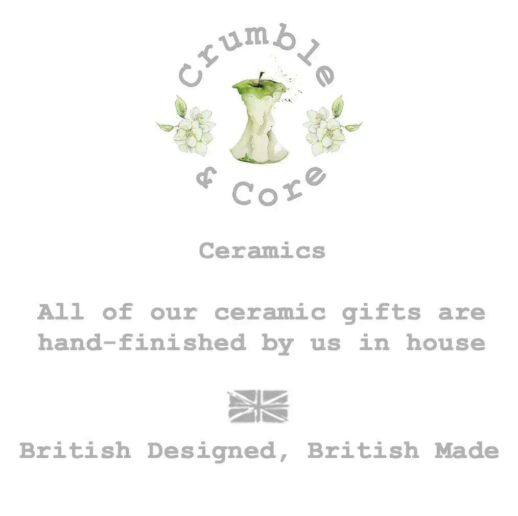 The image is a logo for a company called Crumble & Core, which specializes in ceramics. The logo features an apple with a green stem and leaves, surrounded by white flowers. The company's slogan, "All of our ceramic gifts are hand-finished by us in house", is displayed below the logo. The company's British-designed, British-made tagline is also included in the image.